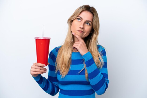Giovane donna uruguaiana che beve soda isolata su sfondo bianco con dubbi