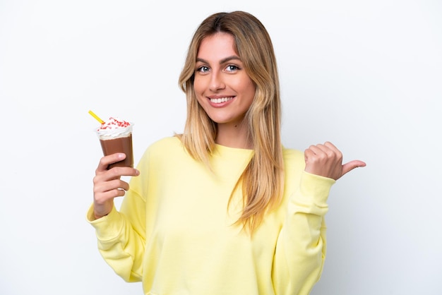 Giovane donna uruguaiana che tiene Frappuccino isolato su sfondo bianco che indica il lato per presentare un prodotto