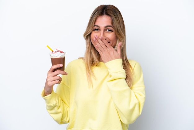 Giovane donna uruguaiana che tiene Frappuccino isolato su sfondo bianco felice e sorridente che copre la bocca con la mano