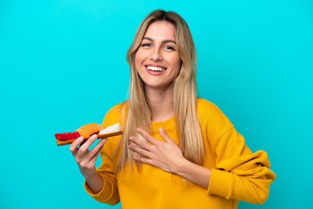 Giovane donna uruguaiana che tiene il sashimi isolato su sfondo blu che sorride molto