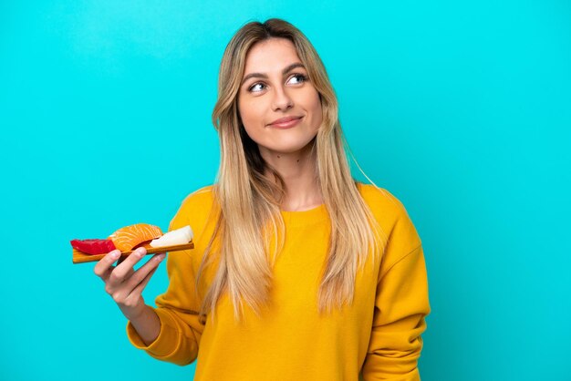 Giovane donna uruguaiana che tiene sashimi isolato su sfondo blu pensando un'idea mentre guarda in alto