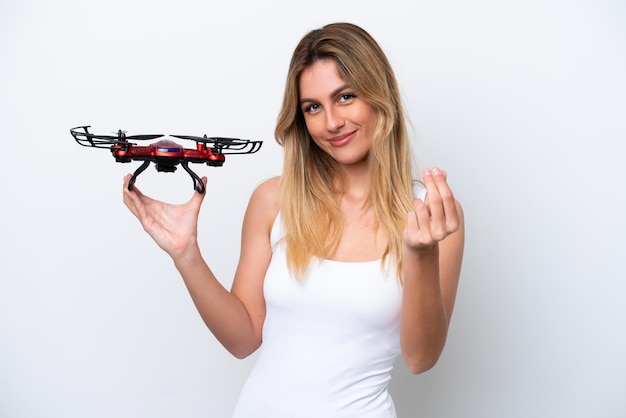 Giovane donna uruguaiana che tiene un drone isolato su sfondo bianco facendo un gesto di denaro