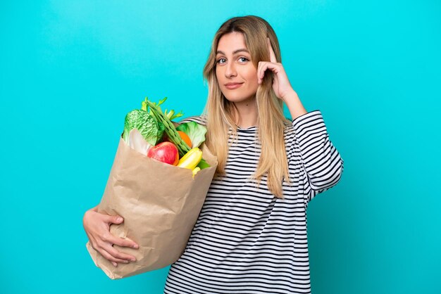 Giovane donna uruguaiana che tiene una borsa della spesa isolata su sfondo blu pensando un'idea