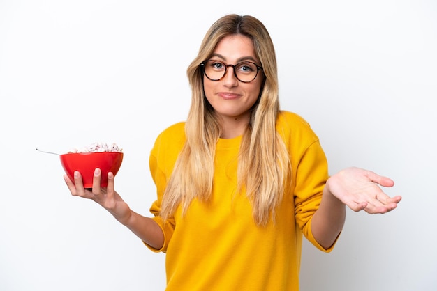 Giovane donna uruguaiana che tiene una ciotola di cereali isolata su sfondo bianco facendo un gesto di dubbi mentre si sollevano le spalle