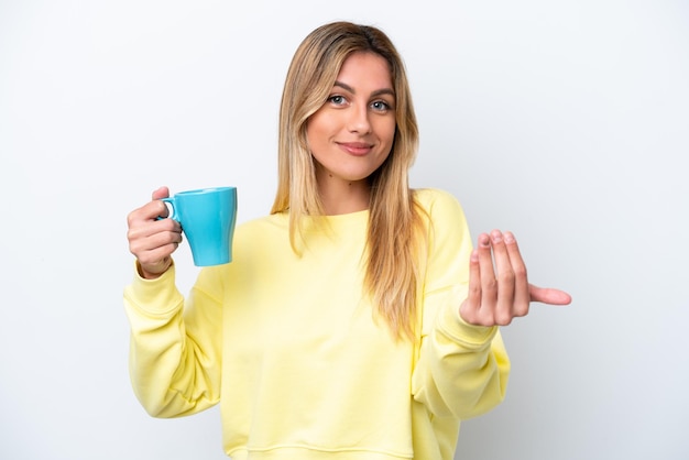 Giovane donna uruguaiana che tiene una tazza di caffè isolata su sfondo bianco che invita a venire con la mano Felice che tu sia venuto