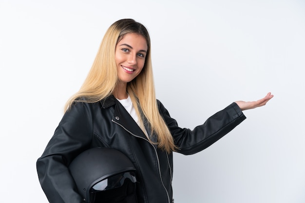 Giovane donna uruguaiana con un casco da motociclista sul muro bianco isolato che estende le mani a lato per invitare a venire