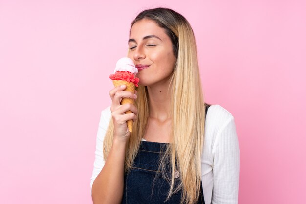 Giovane donna uruguaiana con un gelato di cornetta sopra la parete isolata di rosa della parete