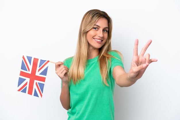 Giovane donna uruguaiana in possesso di una bandiera del Regno Unito isolata su sfondo bianco sorridente e che mostra il segno della vittoria