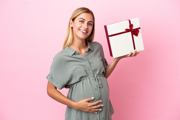 Giovane donna uruguaiana isolata su sfondo blu incinta e in possesso di un regalo