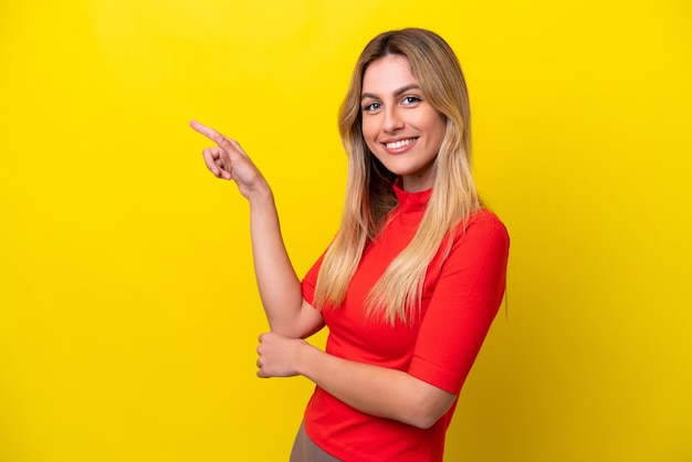 Giovane donna uruguaiana isolata su sfondo giallo che punta il dito di lato