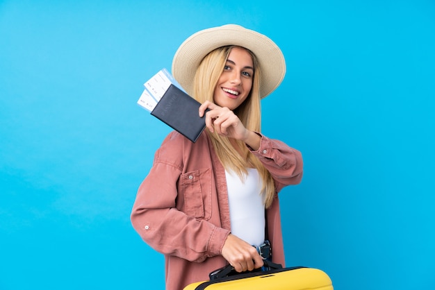 Giovane donna uruguaiana sopra la parete blu isolata in vacanza con la valigia e il passaporto