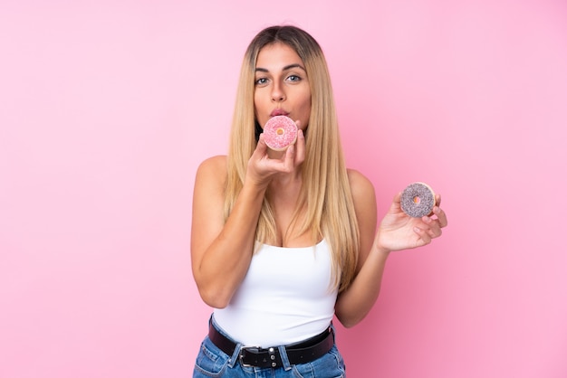 Giovane donna uruguaiana sopra la parete rosa isolata che tiene una ciambella