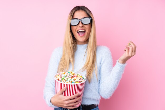 Giovane donna uruguaiana sul muro isolato rosa muro con occhiali 3d e in possesso di un grande secchio di popcorn