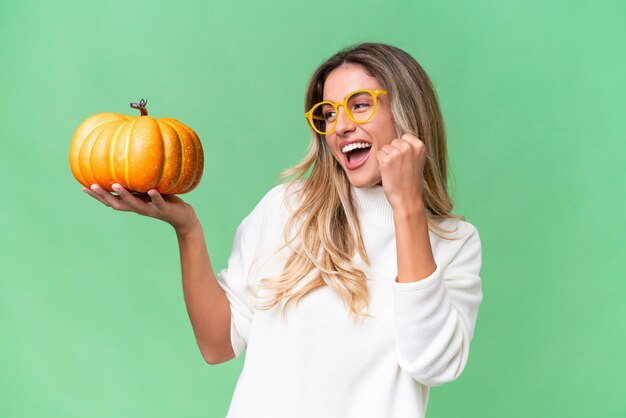 Giovane donna uruguaiana tenendo una zucca su sfondo isolato che celebra una vittoria