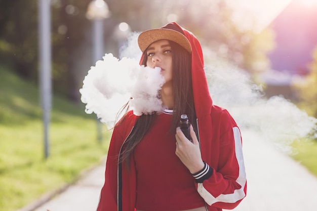 Giovane donna vape ecig femmina abbastanza giovane in cappello nero rosso abbigliamento vape ecig