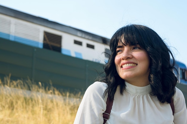 giovane donna venezuelana con i capelli corti e abiti casual in un parco seduto sorridente mentre il treno passa dietro il suo spazio di copia del concetto di viaggio