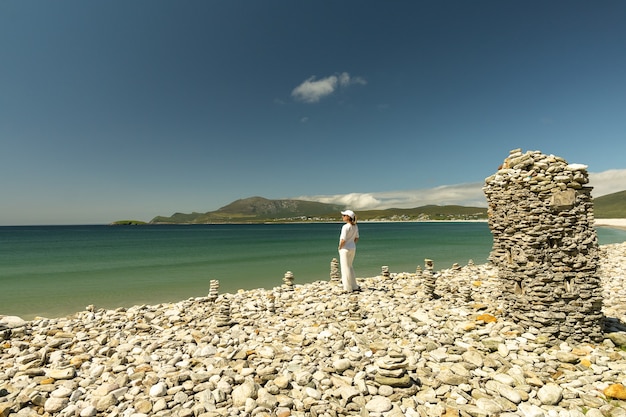 Giovane donna vestita di bianco guardando la spiaggia rocciosa a Keel Beach Achill Island Ireland