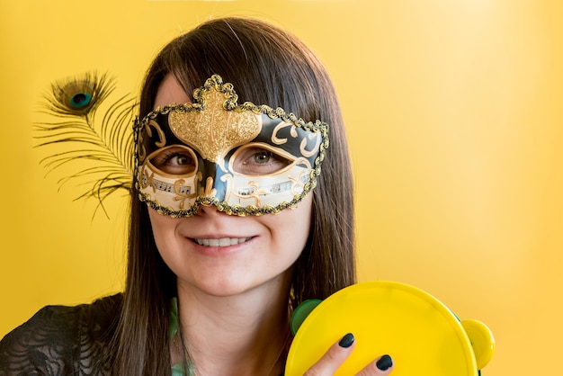 Giovane donna vestita in costume di carnevale che suona il tamburello alla festa di carnevale, sfondo giallo.