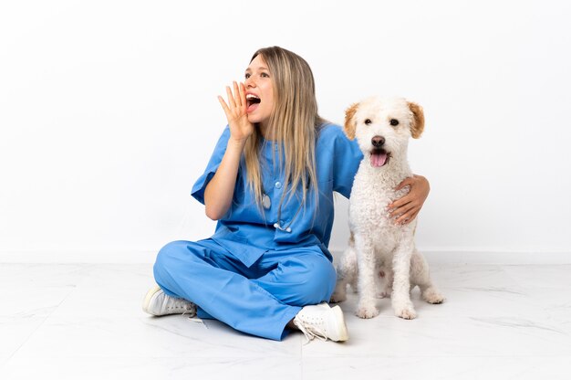 Giovane donna veterinaria con cane seduto sul pavimento gridando con la bocca spalancata di lato