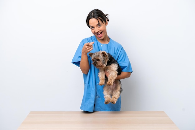 Giovane donna veterinaria con cane su un tavolo isolato su sfondo bianco punta il dito contro di te con un'espressione sicura