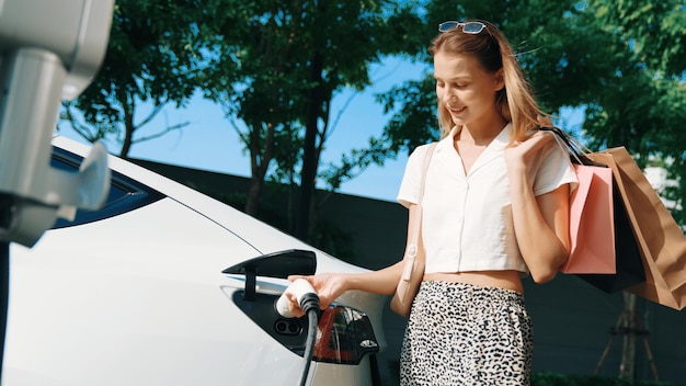 Giovane donna viaggia con un'auto elettrica EV nelle interiorità di una città sostenibile e verde