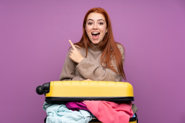 Giovane donna viaggiatore con una valigia piena di vestiti che punta il dito verso il lato