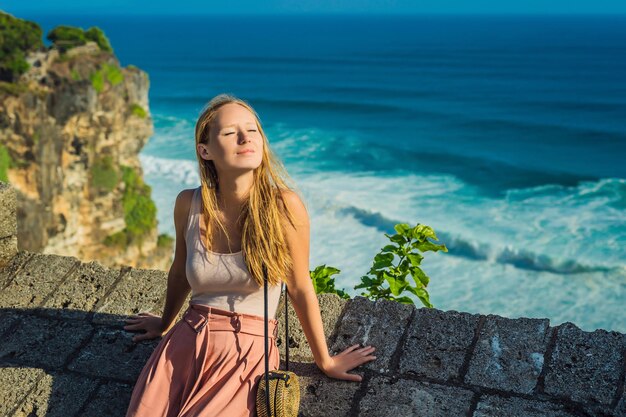 Giovane donna viaggiatore nel tempio di Pura Luhur Uluwatu, Bali, Indonesia. Incredibile paesaggio - scogliera con cielo blu e mare.