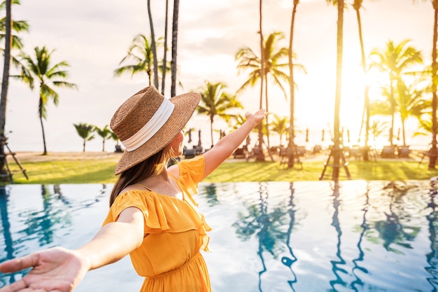 Giovane donna viaggiatrice che si rilassa e si gode il tramonto da una piscina di un resort tropicale mentre viaggia per le vacanze estive summer