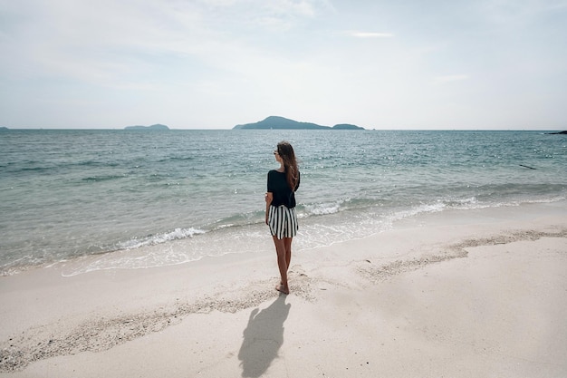 Giovane donna viaggiatrice in gonna a righe e t-shirt verde in piedi vicino al mare blu e guardando all'orizzonte. Bella alba. Phuket. Tailandia