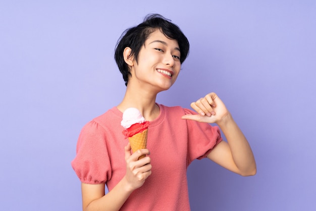 Giovane donna vietnamita con i capelli corti in possesso di un gelato di cornetta sul muro viola orgoglioso e soddisfatto di sé