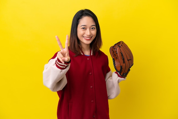 Giovane donna vietnamita del giocatore con il guanto da baseball isolato su fondo giallo che sorride e che mostra il segno di vittoria