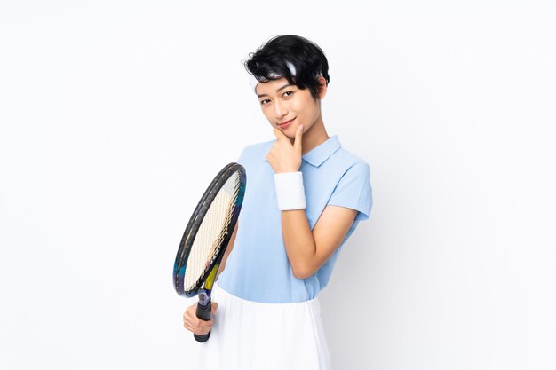 Giovane donna vietnamita del tennis sopra la parete bianca isolata che gioca a tennis e che pensa