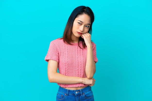 Giovane donna vietnamita isolata su sfondo blu con espressione stanca e annoiata