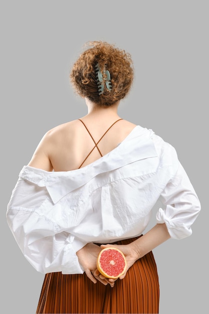 Giovane donna voltata e tiene mezzo pompelmo nelle mani dietro la schiena