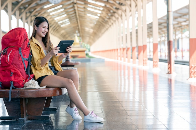 Giovane donna zaino in spalla che utilizza tablet alla ricerca di una destinazione da percorrere seduti alla stazione ferroviaria