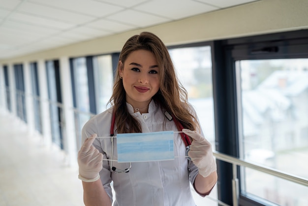 Giovane dottoressa o infermiera che mette una maschera per la protezione contro il coronavirus COVID-19.