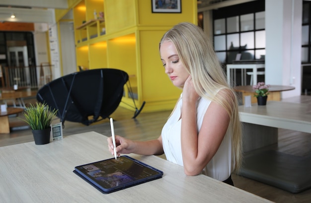 Giovane e allegra donna che lavora su tablet digitale utilizzando internet wireless mentre è seduta rilassata al caffè. Concetto di tempo libero, freelance e lavoro mobile