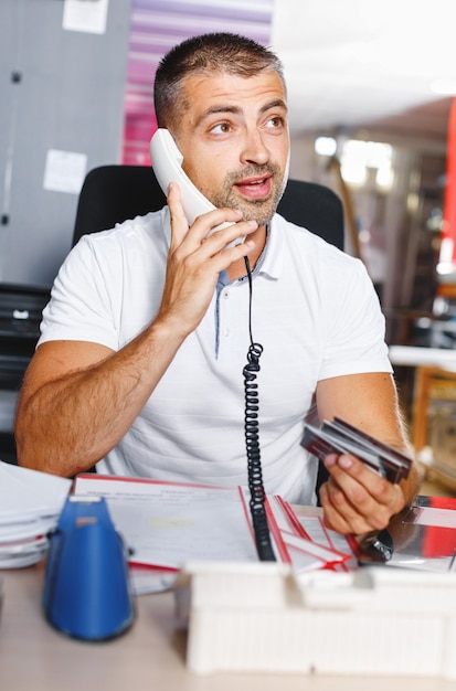 Giovane e ambizioso commerciante di borsa sta facendo un affare al telefono in un ufficio pieno di computer.