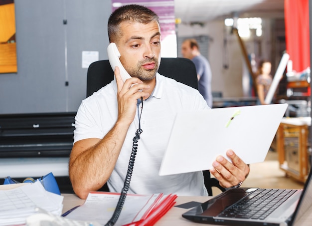 Giovane e ambizioso commerciante di borsa sta facendo un affare al telefono in un ufficio pieno di computer.