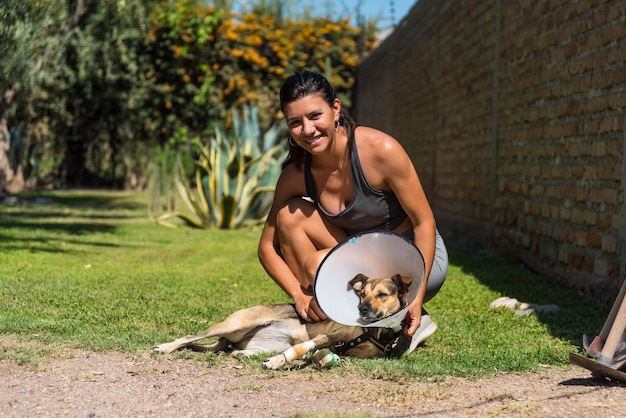 Giovane e bella donna che si prende cura del suo cane ferito sull'erba in una giornata di sole