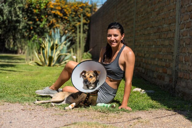 Giovane e bella donna che si prende cura del suo cane ferito sull'erba in una giornata di sole