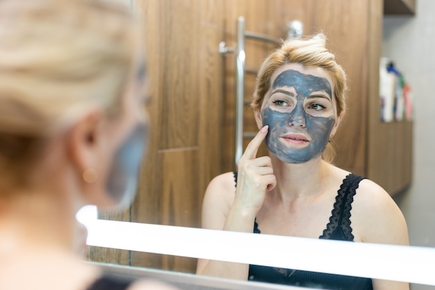 Giovane e bella donna con maschera peel-off nera sul viso dopo la doccia
