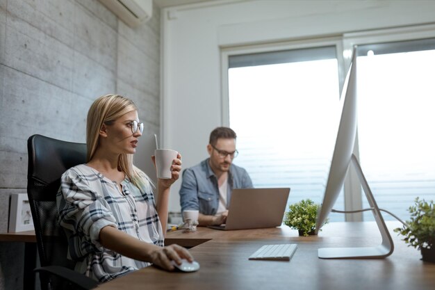 Giovane e bella donna freelance pensierosa che lavora a un nuovo progetto in ufficio. Sta guardando il progetto e sta bevendo il tè.