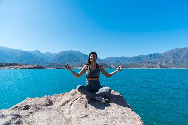 Giovane e bella donna sorridente in un lago tra le montagne yoga