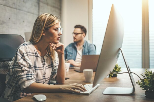 Giovane e bella freelance pensierosa sta lavorando a un nuovo progetto al computer in ufficio.