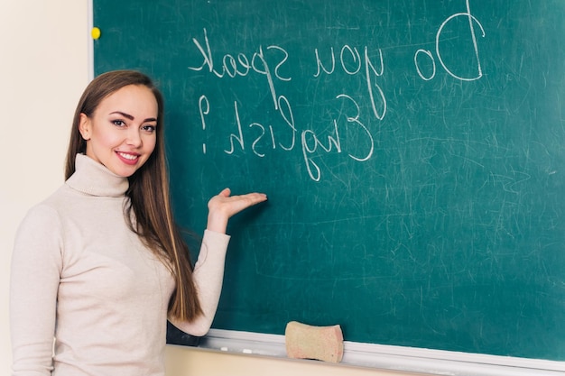 Giovane e bella insegnante in piedi vicino al consiglio e insegnando la lingua inglese in classe Lei sorride in classe di scuola o università Istruzione e concetto di lavoro