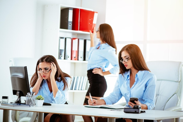 Giovane e bella segretaria multitasking che lavora sodo in ufficio. Sta lavorando al computer, scrivendo sull'agenda e prendendo un raccoglitore allo stesso tempo. Stessa persona in molte posizioni.