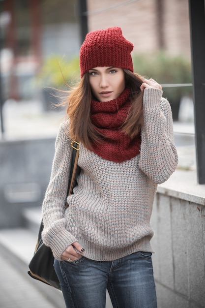 giovane e bella studentessa con un maglione lavorato a maglia, sciarpa rossa e cappello e uno zaino