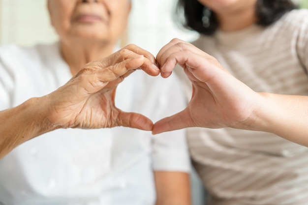 Giovane e donna anziana che fa il concetto di solidarietà del gesto della mano del segno del cuore