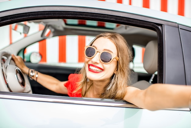 Giovane e donna felice che fa la foto del selfie seduta all'auto sullo sfondo del muro rosso